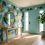 Colorful floral Tidewaltz Wallpaper with blue accents, covering the wall behind a wooden table with books and a round mirror.