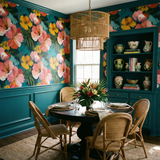 Painter’s Orchard Wallpaper with floral pattern, complementing green wainscoting and a rattan chandelier in a dining room setting.
