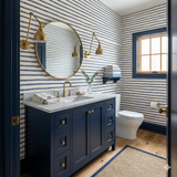 Nautical-themed wallpaper with blue rope pattern on white background; matching navy blue vanity cabinet and golden fixtures are visible.