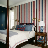 Regatta column wallpaper with red, blue, and beige stripes on the wall behind a four-poster bed.