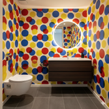 Polychrome pop wallpaper with red, yellow, and blue dots on a dotted background, covering a bathroom.
