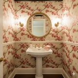 Floral wallpaper with cherry blossom pattern on the wall covering, featuring a gold framed mirror.
