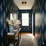 Navy sprig almanac wallpaper with a floral pattern, covering a hallway wall beside a wooden table.