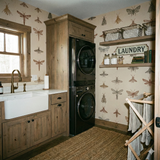 Insects wallpaper with brown and grey moth pattern, from Fieldwarden, covers a laundry room, with wooden shelving and cabinetry.