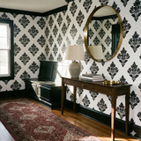 Blackwell Cartouche Wallpaper with black and white pattern, covering a wall with an oval mirror.