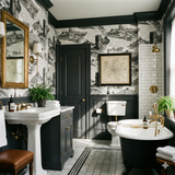 Patterned wallpaper with cityscapes by Meridian Hall, above black wainscoting in a traditional bathroom.