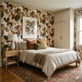 Garden Fragments wallpaper with a floral pattern on the wall, behind a bed with pillows and a throw.
