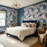 Floral wallpaper by Bluehaven, decorating a bedroom with white bedding, wood furniture, and blue trim.
