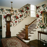 Floral pattern Briarberry Parlour Wallpaper with red and white blooms, displayed on a wall near a staircase.