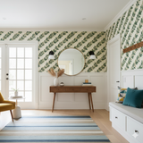 Green wallpaper with green leaf pattern by York Wallcoverings, decorating an entryway with a mirror and wood console table.
