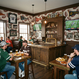 Gridiron Etching Room Wallpaper with football pattern, decorating a bar with televisions, drinks, and people wearing sports jerseys.
