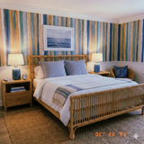 Drifted Strata Wallpaper with blue, green, and yellow vertical stripes behind rattan bed frame.