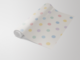 Roll of wallpaper with pastel polka dots on a cream background.